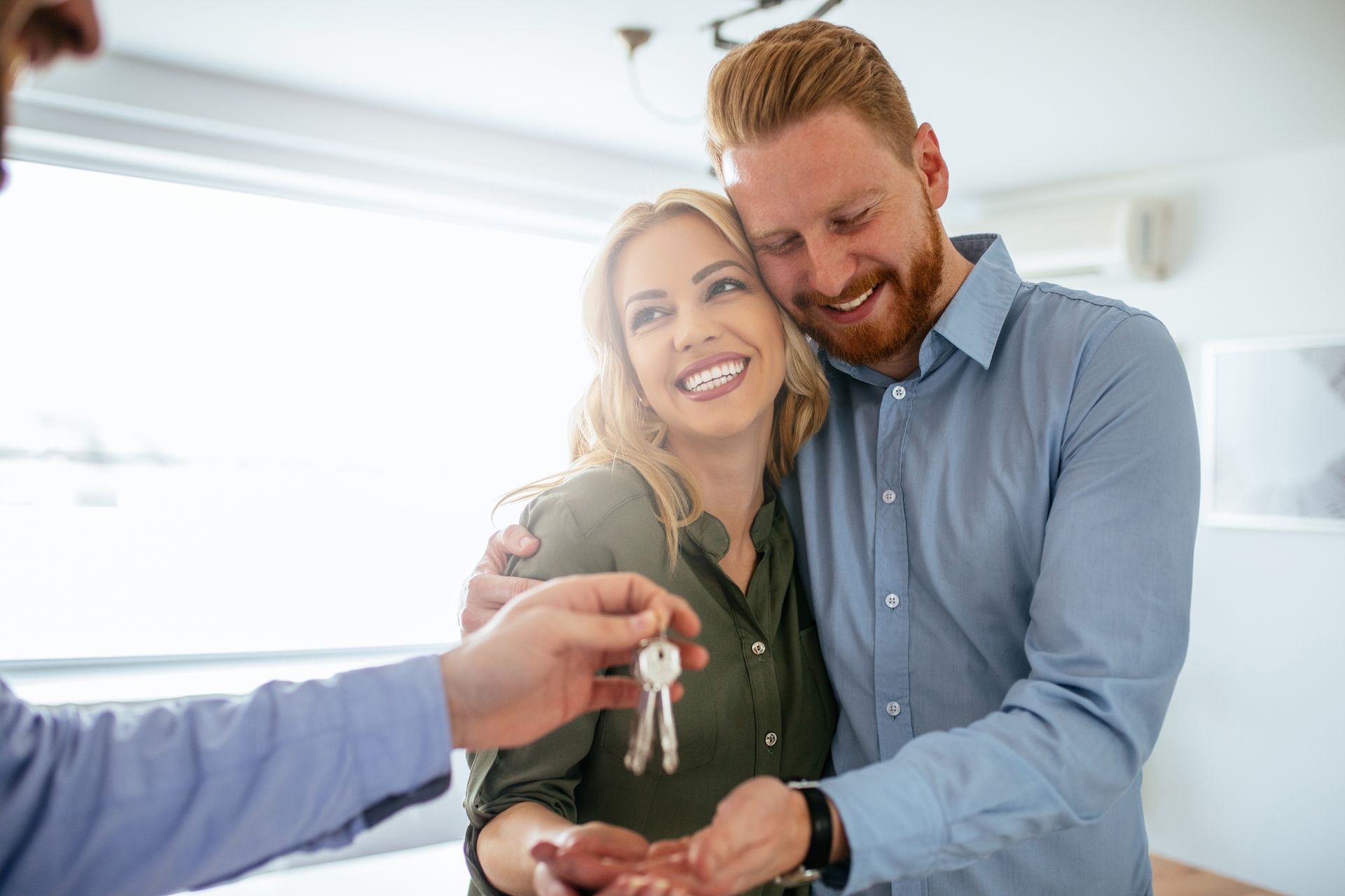 Une personne remet les clés d'une maison à un couple souriant.